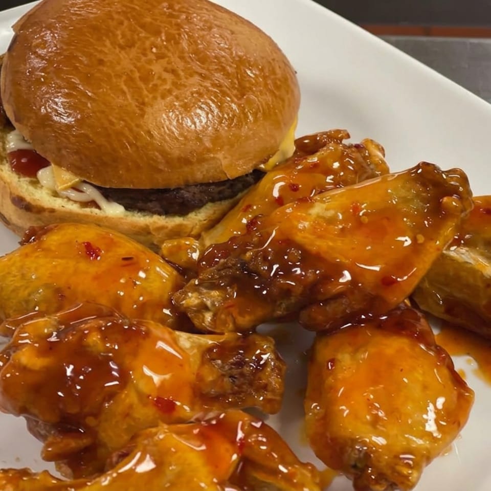 Glazed chicken wings served with a brioche burger on a white plate.