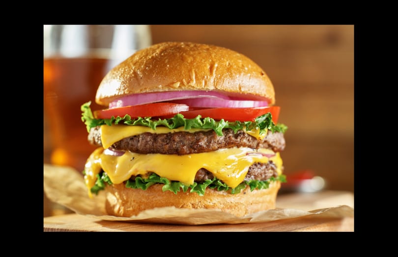 A double cheeseburger from & Burger with lettuce, tomato, and red onion on a bun.
